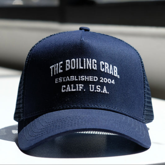 Navy blue cap with 'The Boiling Crab' embroidered text and red logo tag.  